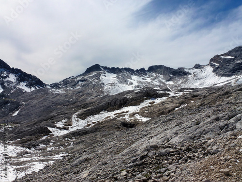 View of rocky rocky mountain slopes partially covered with snow. Above them is a sky with white clouds. Winter landscape and wildlife