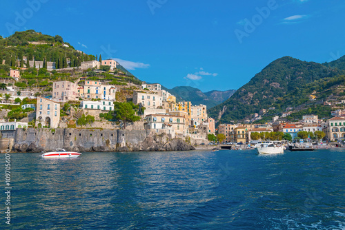 This image showcases Minori on the Amalfi Coast, with its charming seaside houses, tranquil beach, and lush green hills, bathed in the warm Mediterranean light.