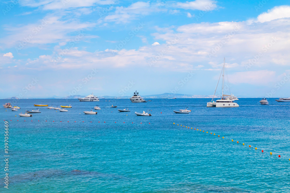 The photo captures a view of Capri from the water, showcasing the island's iconic cliffs, colorful buildings, and lush greenery set against the clear blue sea and sky.