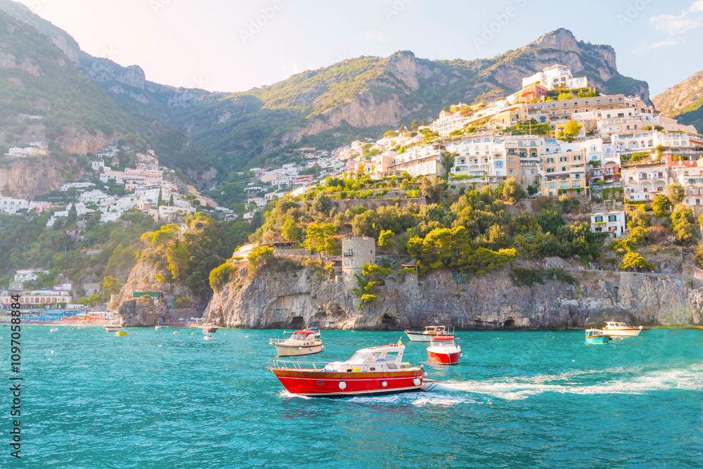 Obraz premium The photo captures a sunny view of Amalfi, showcasing the town's colorful buildings, steep cliffs, and vibrant coastline under a clear blue sky on a bright day.
