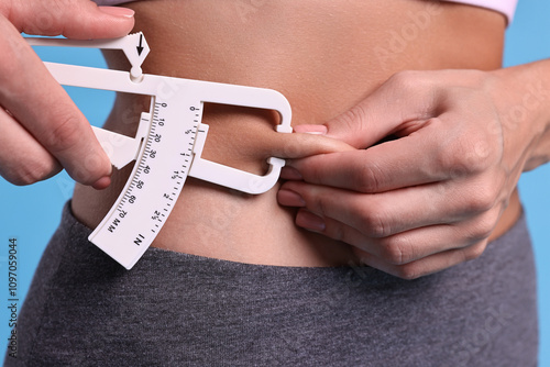 Woman measuring body fat with caliper on light blue background, closeup