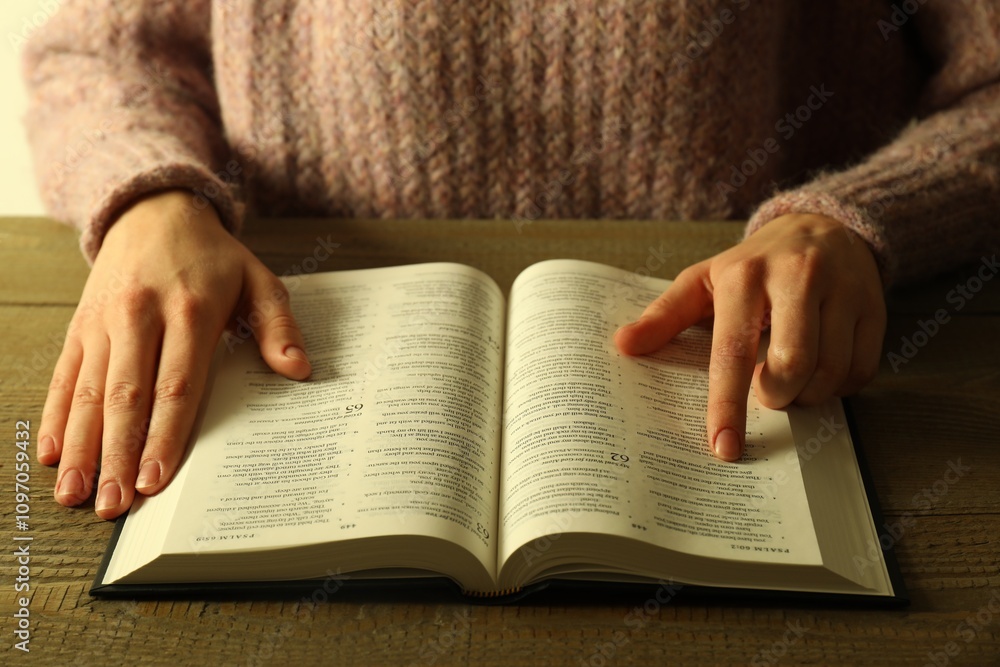 Woman reading Holy Bible in English language at wooden table, closeup Woman reading Holy Bible in English language at wooden table, closeup