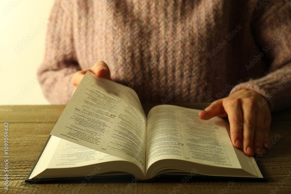 Woman reading Holy Bible in English language at wooden table, closeup Woman reading Holy Bible in English language at wooden table, closeup