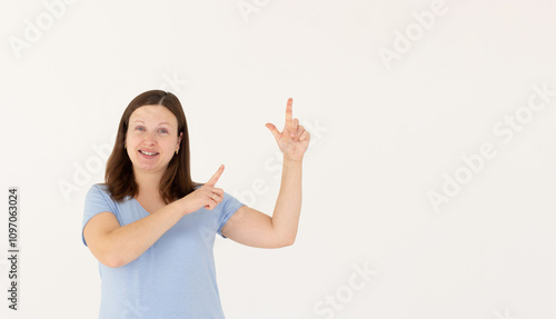 Hey look. Smiling pretty female model pointing fingers right at empty space and inviting to check it out, showing advertisement on white background.