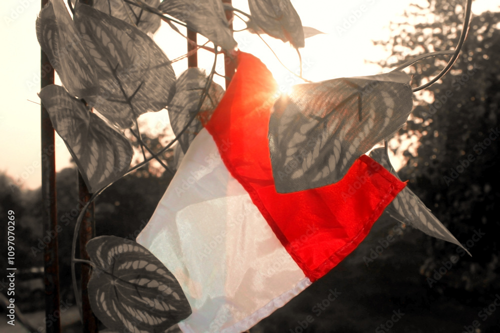 Obraz premium Indonesian flag mounted on an iron bar and surrounded by leaves. The coloring focuses only on the flag.