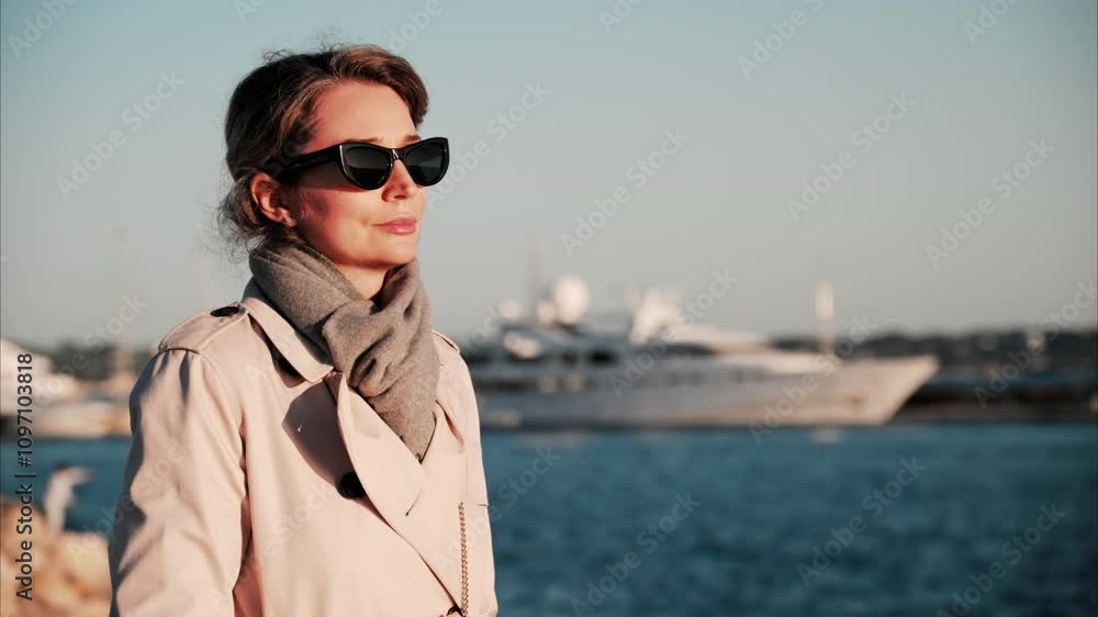 Woman wearing sunglasses and a trench coat while looking at the sea in France Woman wearing sunglasses and a trench coat while looking at the sea in France