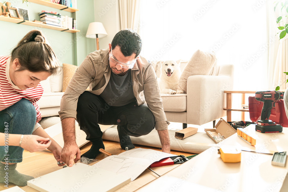 Happy Couple Assembles Furniture as a Team, Girl Reads Instructions and Boy Tightens Screw with a Drill. Moving into New Apartment, Couple Assemble Shelf. Happy Couple Assembles Furniture as a Team, Girl Reads Instructions and Boy Tightens Screw with a Drill. Moving into New Apartment, Couple Assemble Shelf.