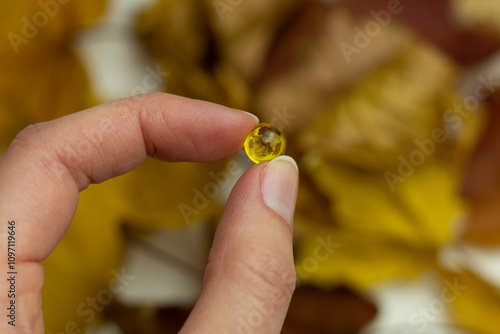 Concept of autumn supplementation. Closeup of a vitamin D capsule and yellow leaves.