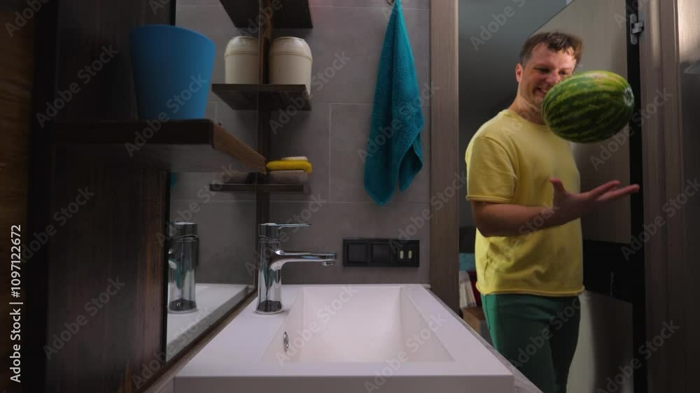 A young man with a smile washes a watermelon under the water tap in the kitchen, washing the watermelon peel in the washbasin in a modern design apartment. Slow motion A young man with a smile washes a watermelon under the water tap in the kitchen, washing the watermelon peel in the washbasin in a modern design apartment. Slow motion