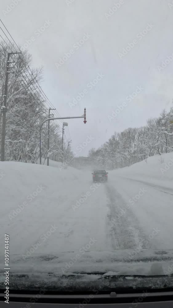 VERTICAL: Frozen windshield and cloudy sky accompany driving in challenging weather conditions with heavy snow. Road lined with snowy trees and distinctive arrow signs during winter driving in Japan VERTICAL: Frozen windshield and cloudy sky accompany driving in challenging weather conditions with heavy snow. Road lined with snowy trees and distinctive arrow signs during winter driving in Japan