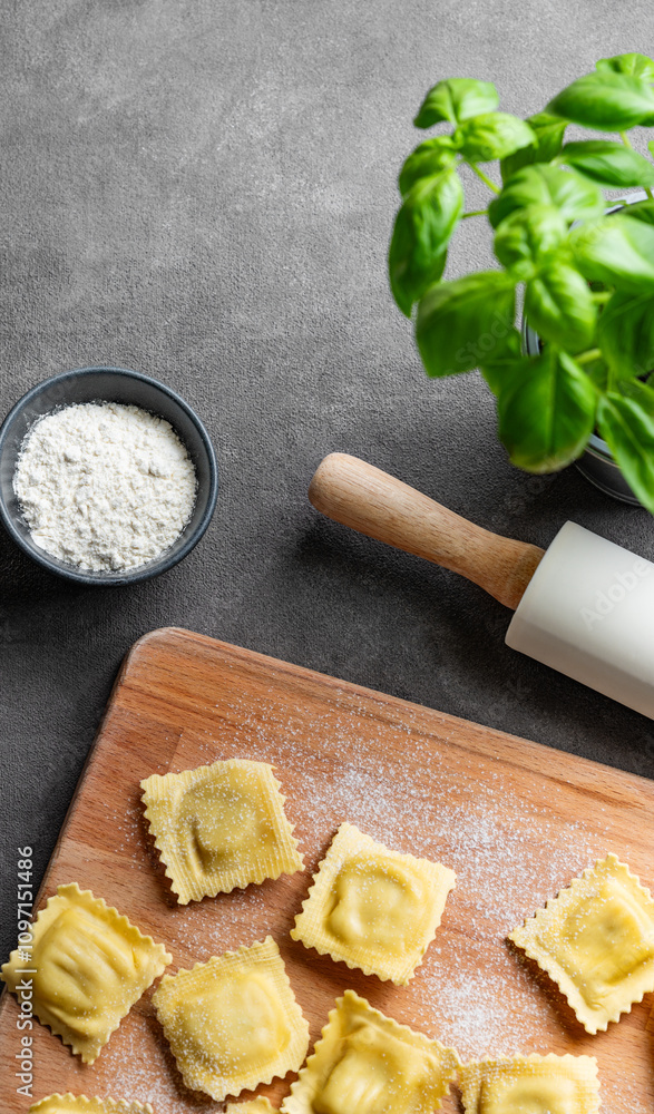 Homemade pasta ravioli with filling on wooden cutting board on dark background with flour, basil and rolling pin. Homemade pasta ravioli with filling on wooden cutting board on dark background with flour, basil and rolling pin.