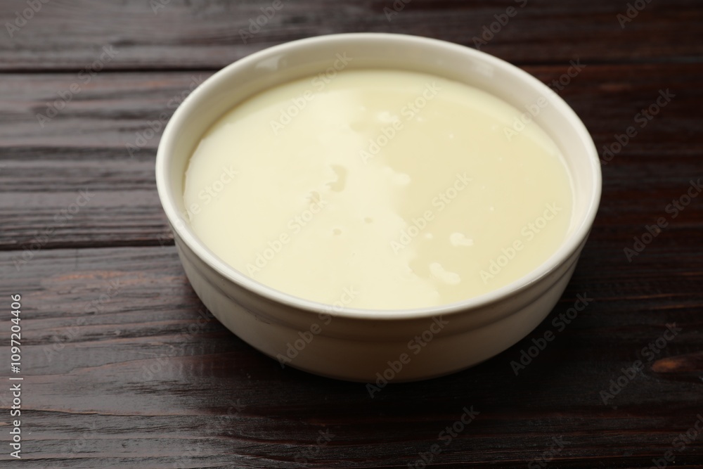 Condensed milk in bowl on wooden table, closeup Condensed milk in bowl on wooden table, closeup
