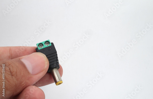 A male DC jack with green screw connection held in hand on white background. photo