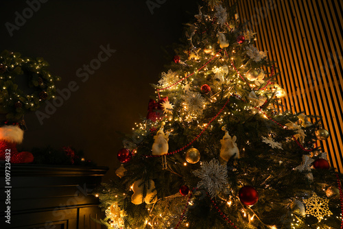 Christmas tree with festive decor in dark room, low angle view