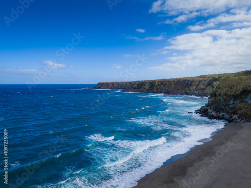 Aerial drone view of Azores islands coast with black sand beach. Praia dos Moinhos landscape in Sao Miguel, Portugal. Atlantic ocean shore with cliffs