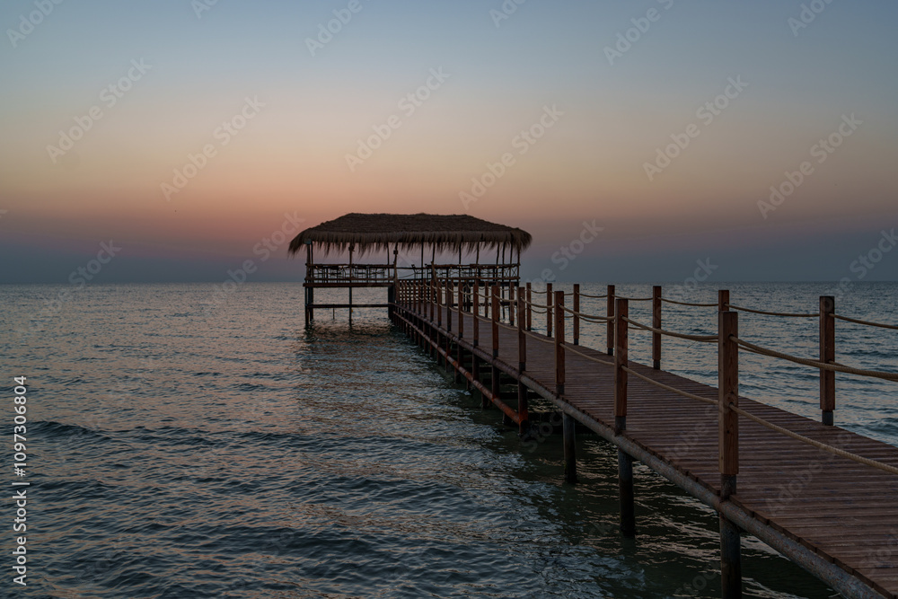 Fototapeta premium A beautiful view of the sunrise, sunset over the sea horizon with a pier in the foreground