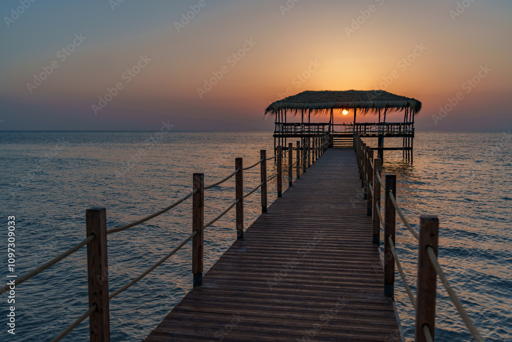 Fototapeta premium A beautiful view of the sunrise, sunset over the sea horizon with a pier in the foreground