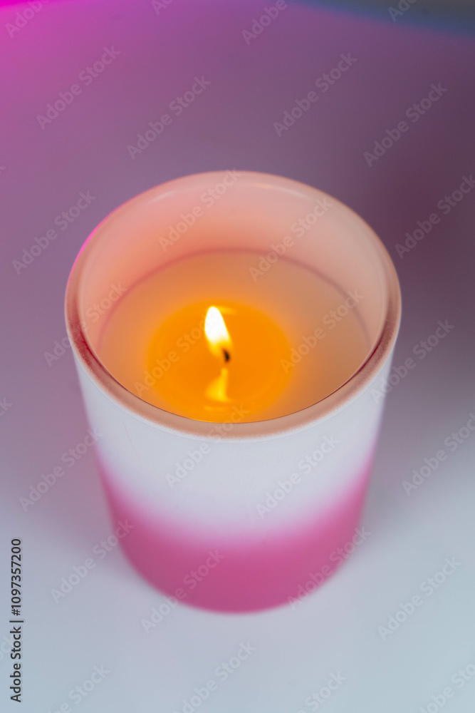 A glowing candle on a table against a pink and purple background. A glowing candle on a table against a pink and purple background.