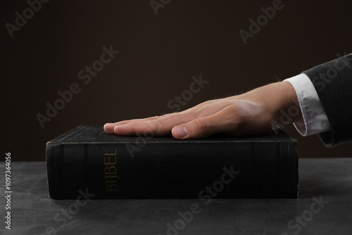 Man taking oath with his hand on Bible at black table, closeup