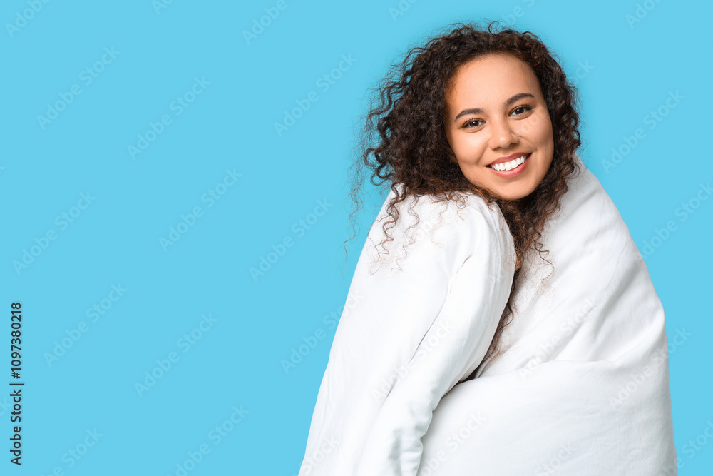 Beautiful young happy African-American woman in pajamas with blanket on blue background Beautiful young happy African-American woman in pajamas with blanket on blue background