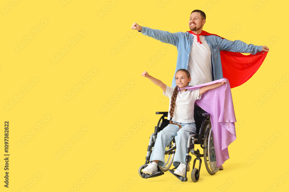 Little girl in wheelchair and her father with superhero capes on yellow background Little girl in wheelchair and her father with superhero capes on yellow background