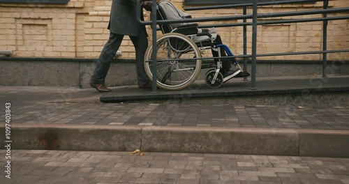 Elderly husband pushes wife in wheelchair along special ramp