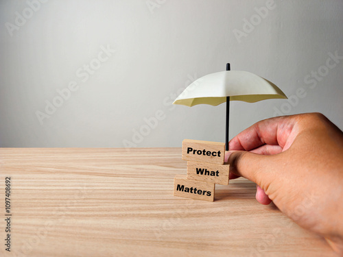 A hand holds a miniature umbrella over wooden blocks reading 