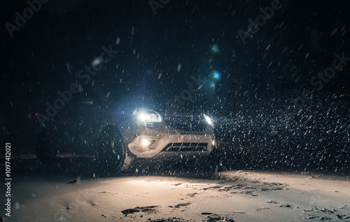 A car parked on a snowy beach at night, illuminated by bright headlights during a winter storm photo