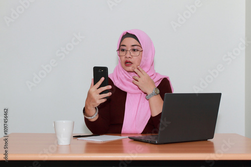 An Asian Muslim lady looks shock while reading something on her smartphone.