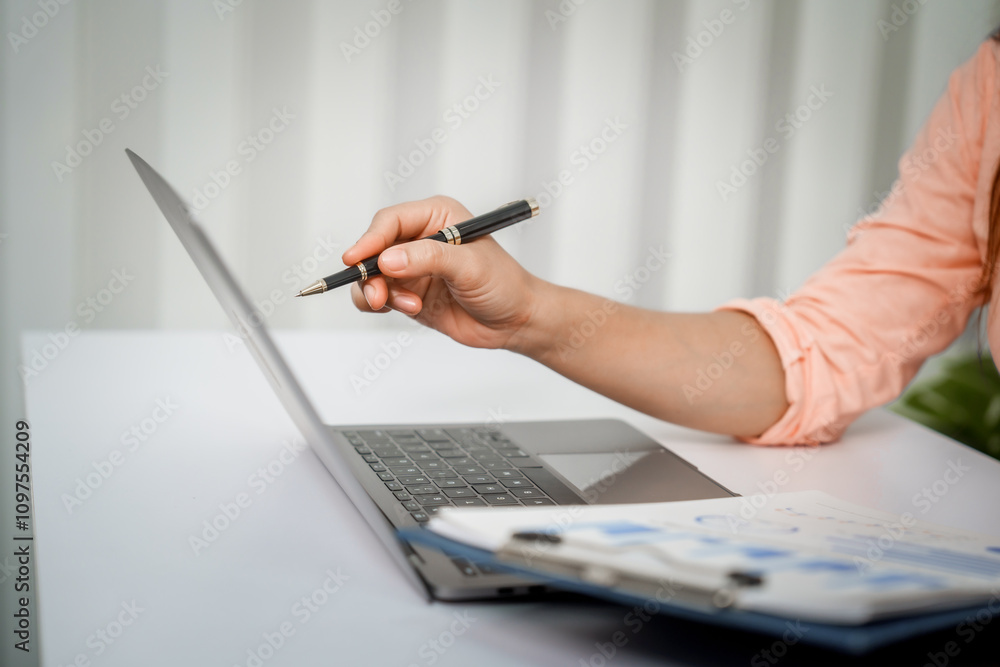 Fototapeta premium A close-up of a businesswoman working on a laptop in an office. As an accountant, she records financial data, verifies documents, manages income and expenses, ensuring accurate financial reporting