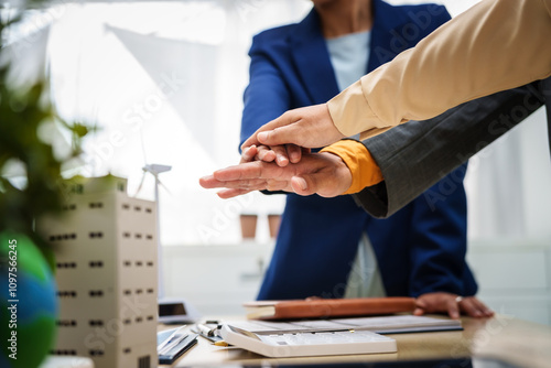 Asian business professionals in collaborate at desk with building models, planning sustainable projects solar panels, electric cars, wind turbines, eco-friendly practices and clean energy solutions.