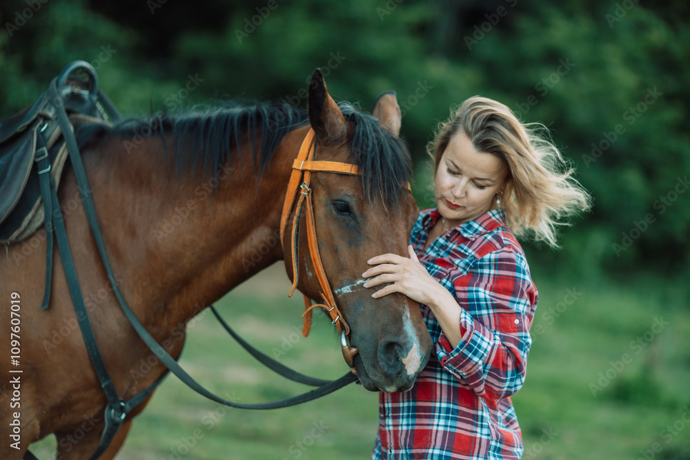 Obraz premium Happy blonde with horse in forest. Woman and a horse walking through the field during the day. Dressed in a plaid shirt and black leggings.