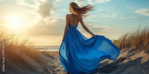 A woman gracefully adorned in a flowing blue gown stands by a windswept shoreline, her dress dramatically catching the breeze, under a vibrant sky. photo