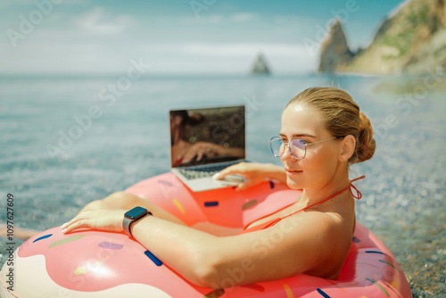 Woman laptop sea. Freelancer woman in sunglases floating on an inflatable big pink donut with a laptop in the sea. People summer vacation rest lifestyle concept photo