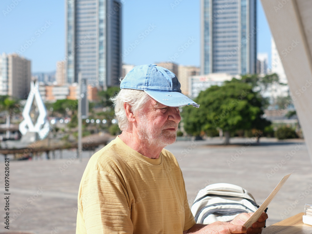 Smiling relaxed tourist man sitting at cafe table looking at menu, traveler bearded retiree sightseeing Tenerife in a sunny day, city life in background Smiling relaxed tourist man sitting at cafe table looking at menu, traveler bearded retiree sightseeing Tenerife in a sunny day, city life in background