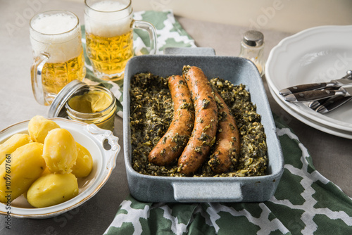 Oldenburger Grünkohl mit Pinkel Kohlwurst in Schale, Salzkartoffeln, Senf und Bier auf gedeckten grau Tisch mit grün Tuch, Teller, Besteck rustikal  photo