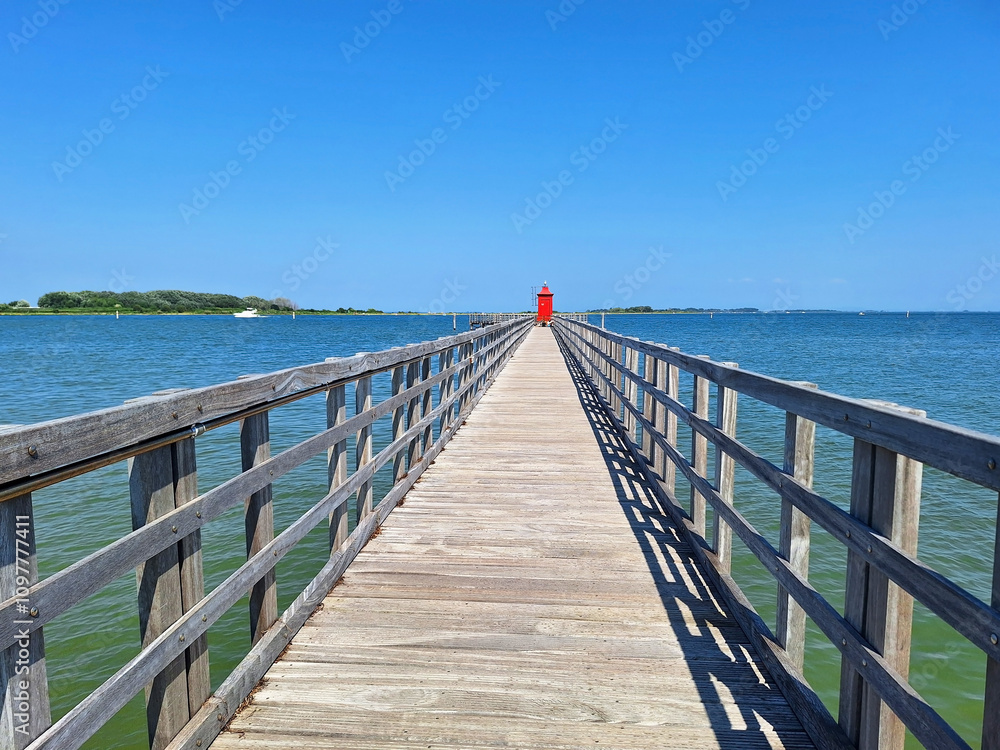 Red lighthouse far from the shore. Wooden bridge leading to the red lighthouse in Lignano Sabbiadoro. Red lighthouse far from the shore. Wooden bridge leading to the red lighthouse in Lignano Sabbiadoro.
