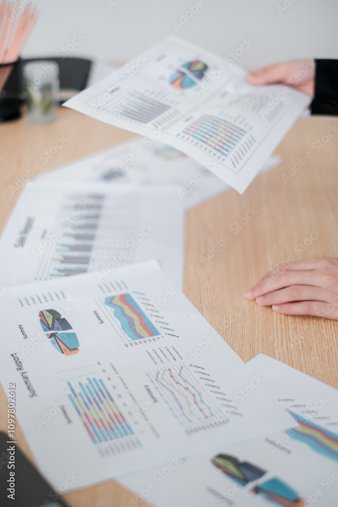 Obraz premium Close-up of hands analyzing financial graphs and charts on a wooden table during a business meeting.