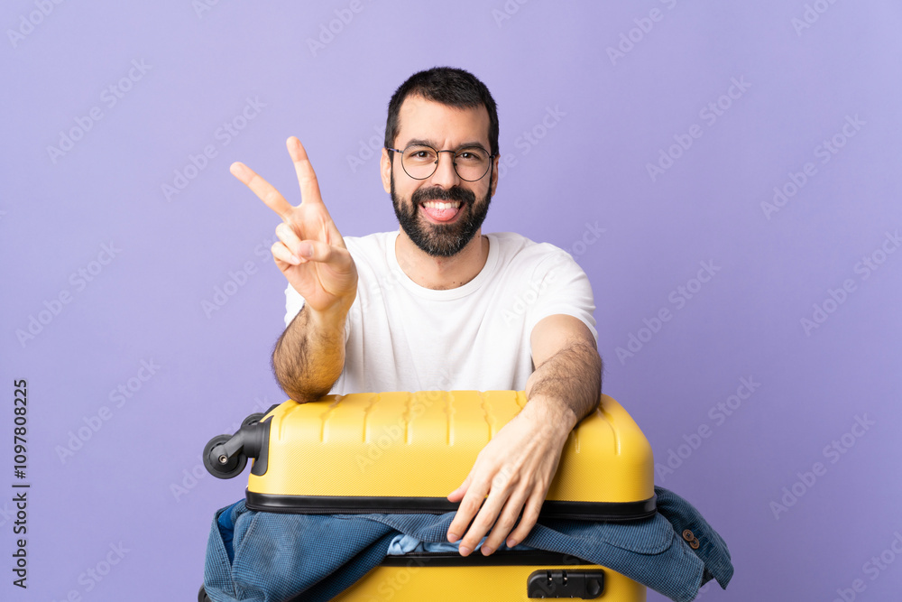 Traveler caucasian man with a suitcase full of clothes over isolated purple background smiling and showing victory sign Traveler caucasian man with a suitcase full of clothes over isolated purple background smiling and showing victory sign