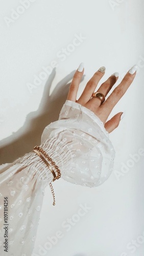 Feminine hand with white manicure wearing rings and bracelet against white dotted sleeve