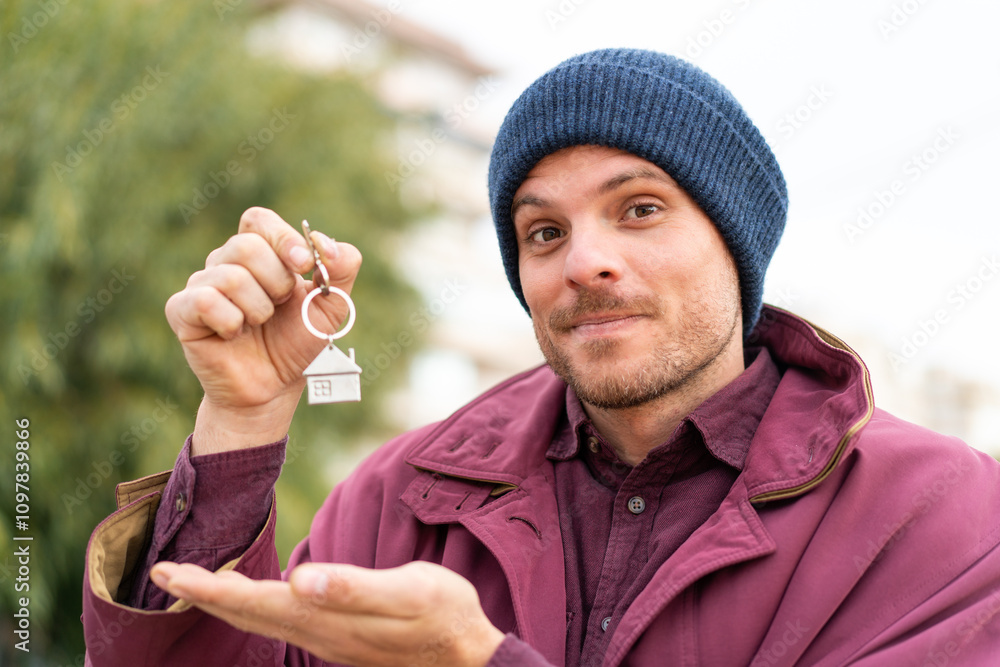 Young caucasian man holding home keys at outdoors Young caucasian man holding home keys at outdoors