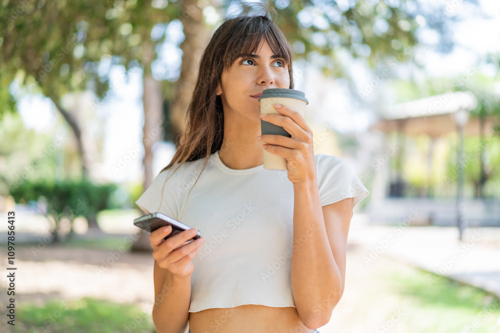 Young woman at outdoors using mobile phone and holding a coffee Young woman at outdoors using mobile phone and holding a coffee