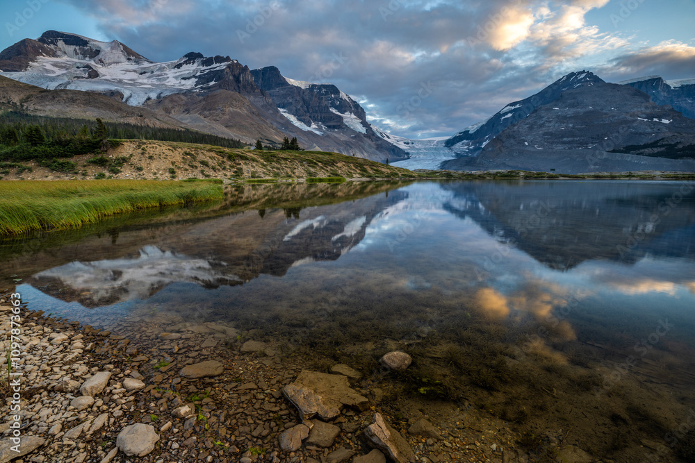 Naklejka premium The panoramic view of snowy mountain and colorful clouds with lake reflections at ice field center of Jasper National Park. Famous Athabasca glacier in Canada.