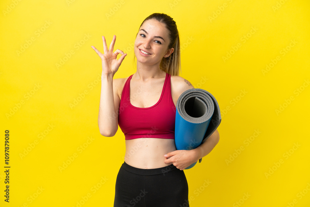 Young sport woman going to yoga classes while holding a mat showing ok sign with fingers Young sport woman going to yoga classes while holding a mat showing ok sign with fingers