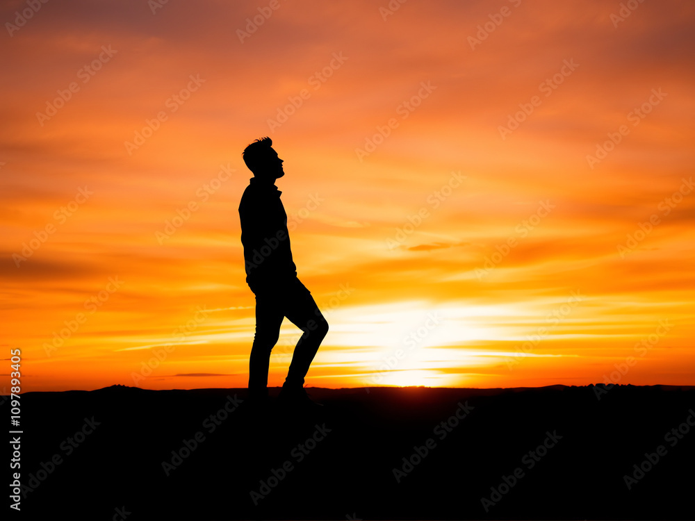 Silhouette of a man standing on a hilltop, gazing at a vibrant sunset in the background. Silhouette of a man standing on a hilltop, gazing at a vibrant sunset in the background.