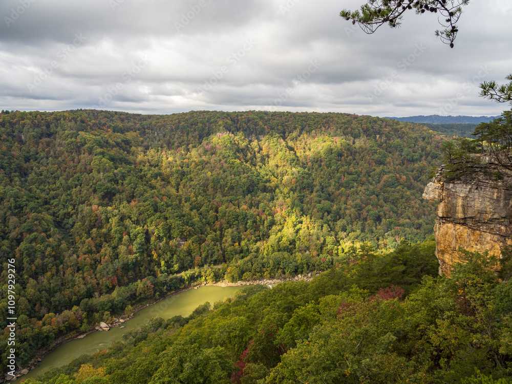 The mountainside at New River Gorge National Park comes alive in fall colors as sunlight highlights the vibrant scene above the tranquil water below. The mountainside at New River Gorge National Park comes alive in fall colors as sunlight highlights the vibrant scene above the tranquil water below.