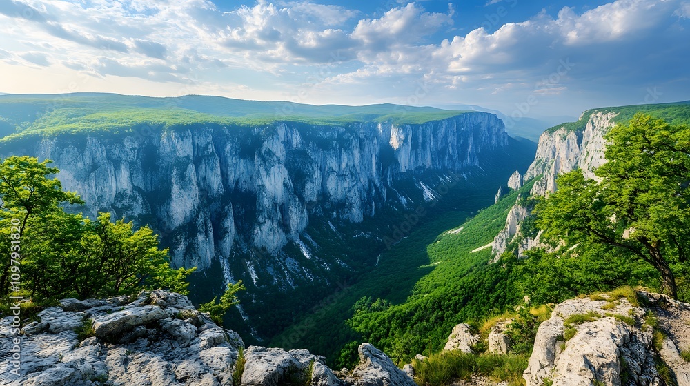 Fototapeta premium Stunning panoramic view of a green valley surrounded by towering cliffs and blue skies.