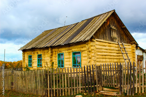 Traditional wooden log cabin with blue windows and wooden fence in rural village showing authentic rustic architecture photo