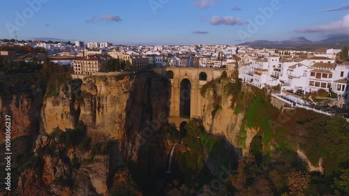 Aerial view of Ronda, Spain, showcasing Puente Nuevo bridge, whitewashed buildings, and a bullring at sunset with a golden glow over the city.