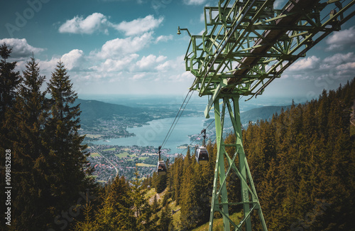 Seilbahn fährt von der Bergstation am Wallberg zu einem See hinab. Tegernsee.Wolken am blauen Himmel. Weiter Blick in den Horizont